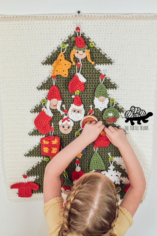 Girl hanging crochet Christmas ornaments on a advent calendar.