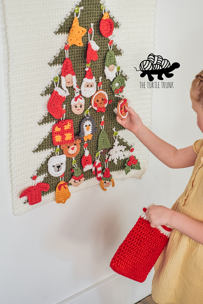 Girl hanging crochet Christmas ornaments on a advent calendar.