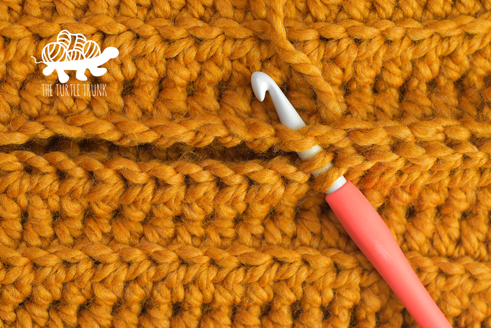 Photo shows a close up of the Easy Breezy Super Chunky Bun Beanie crochet pattern being seamed up with yellow yarn.