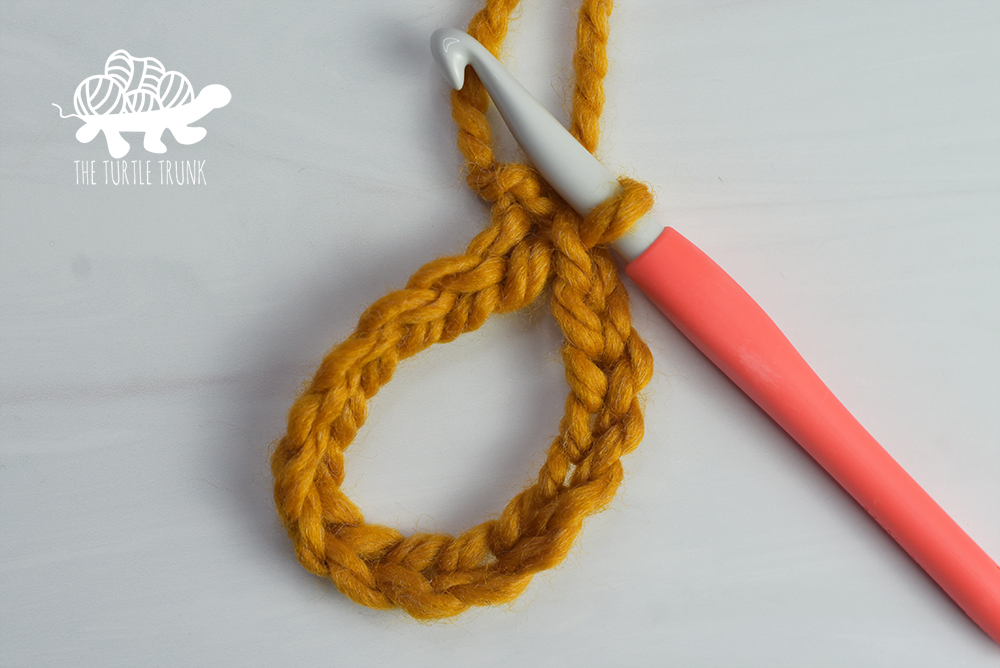 Photo shows a crochet hook and a crochet chain forming a loop with yellow yarn.