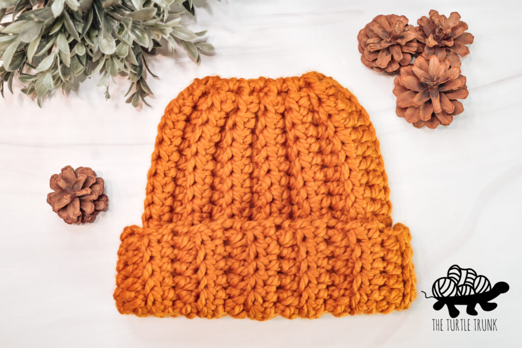 Photo shows a yellow, crochet bun beanie laying on a white surface.