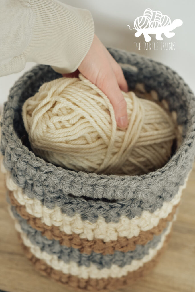 Closeup of a hand placing yarn into a crochet basket.