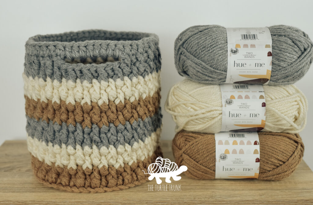 A crochet basket sitting on a desk beside 3 skeins of matching yarn.