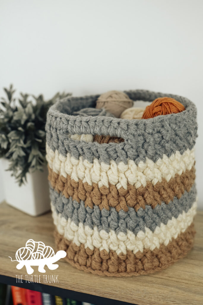 A crochet basket sitting on a desk with balls of yarn inside it.