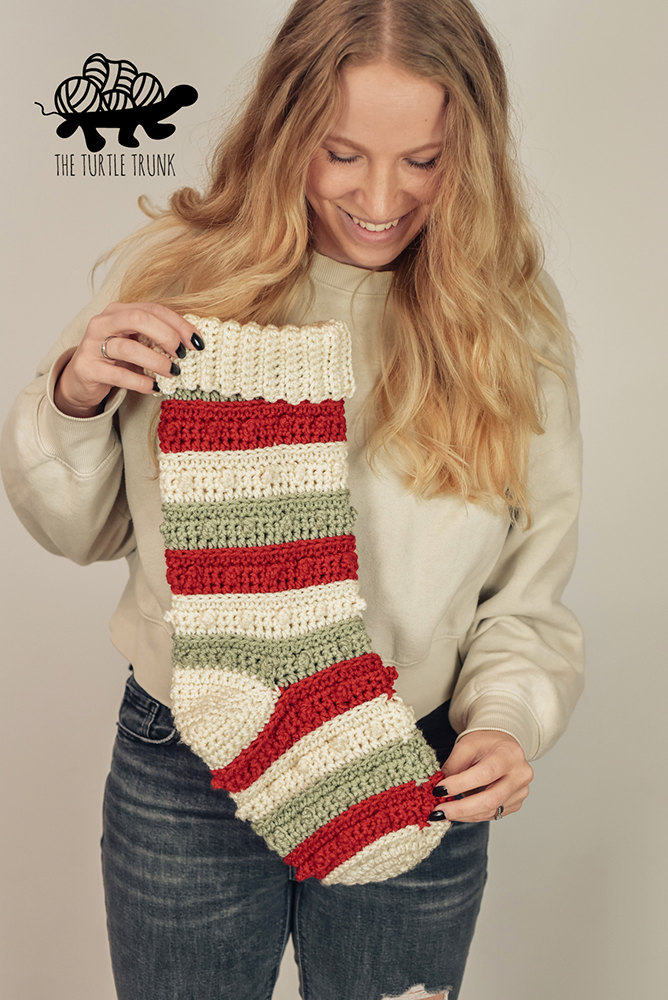 A woman holding a red, white, and green striped crochet Christmas Stocking.