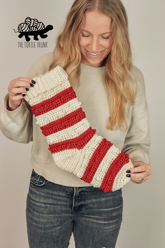 A woman holding a red and white striped crochet Christmas Stocking.