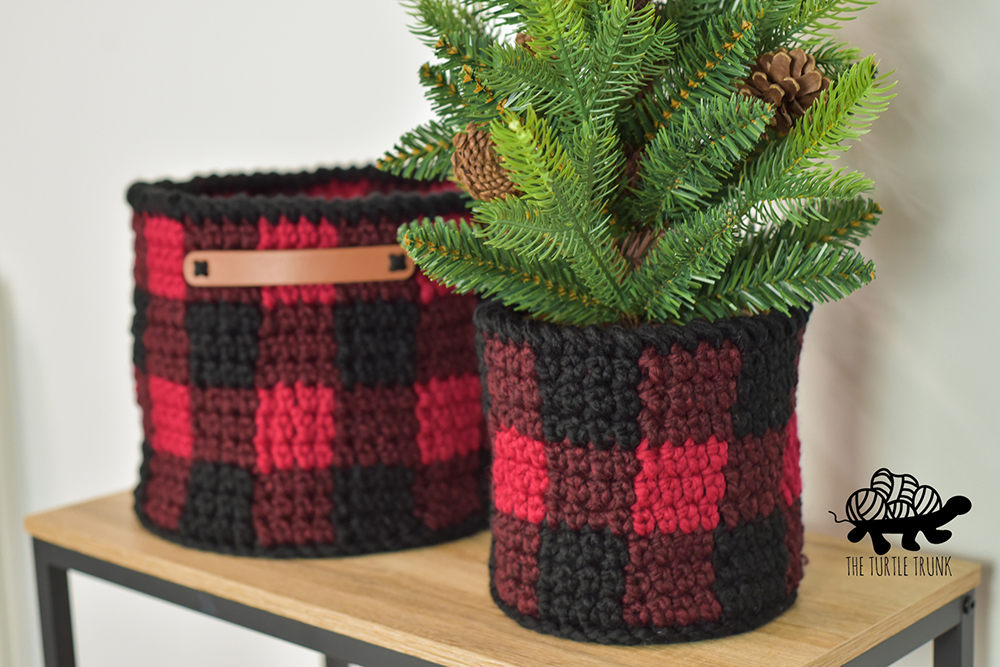 2 plaid crochet baskets sitting on a table.