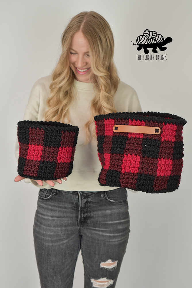 Woman holding 2 plaid crochet baskets.