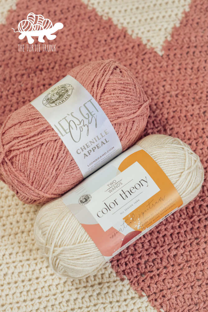 Pink and white yarn laying on a crochet blanket.