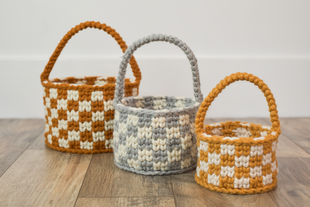 Photo show 3 crochet baskets with a checkered design, sitting on the ground.