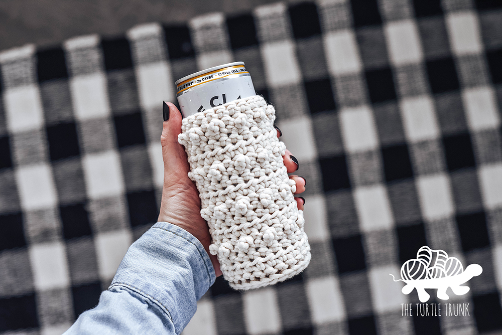 Hand holding a skinny can with a crochet cozy on it.