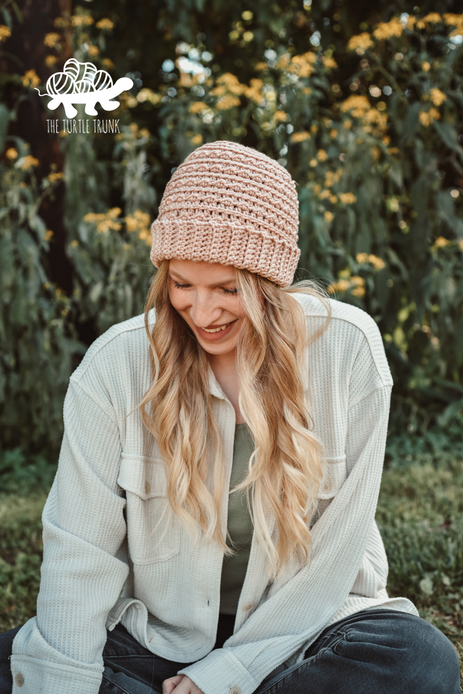 Woman sitting outside, wearing a pink, crochet beanie.