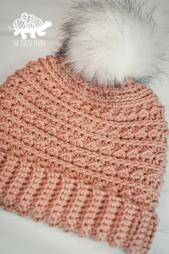 A photo of a pink, crochet beanie with a white, faux fur, pom pom.