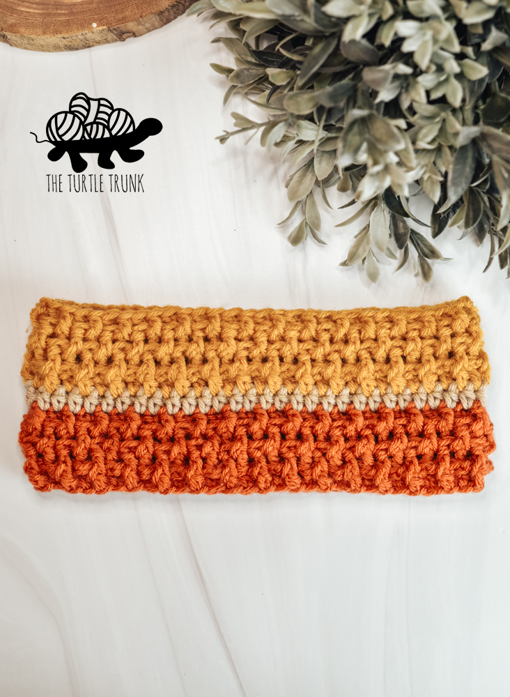 A orange, beige, and yellow stripe, crochet headband on a white surface.