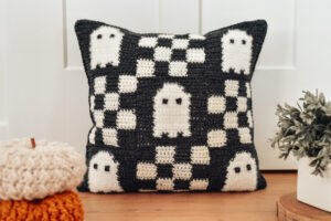 A black and white crochet pillow with a checkered pattern and ghosts on it.