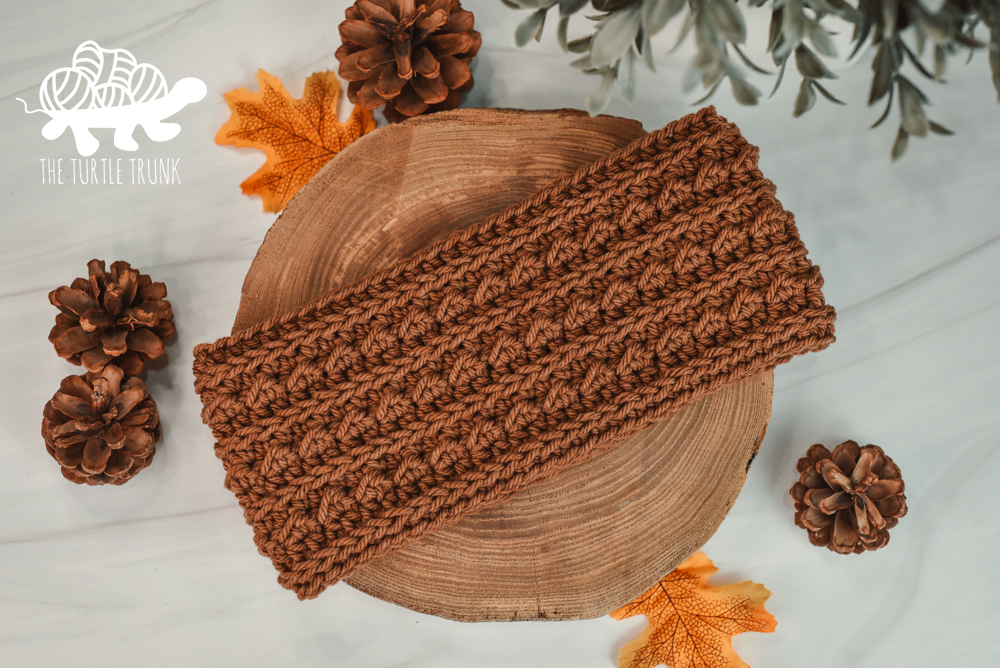 A brown, crochet headband laying on a white surface.
