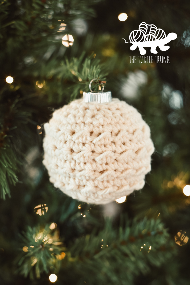 A white, crochet Christmas ornament hanging on a tree.