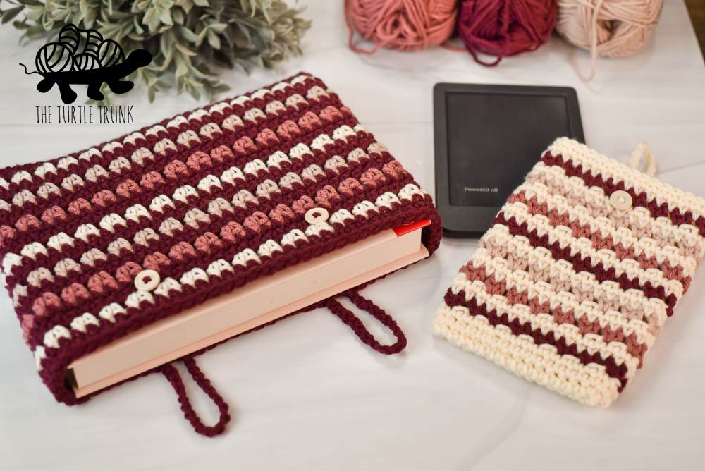 A crochet e-reader and book sleeve laying on a white surface.