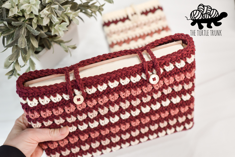 A hand holding a crochet book sleeve with a book in it.