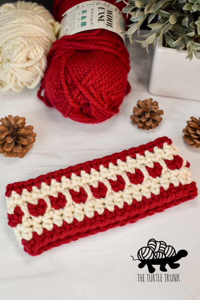 A red and white, crochet ear warmer with hearts on it.