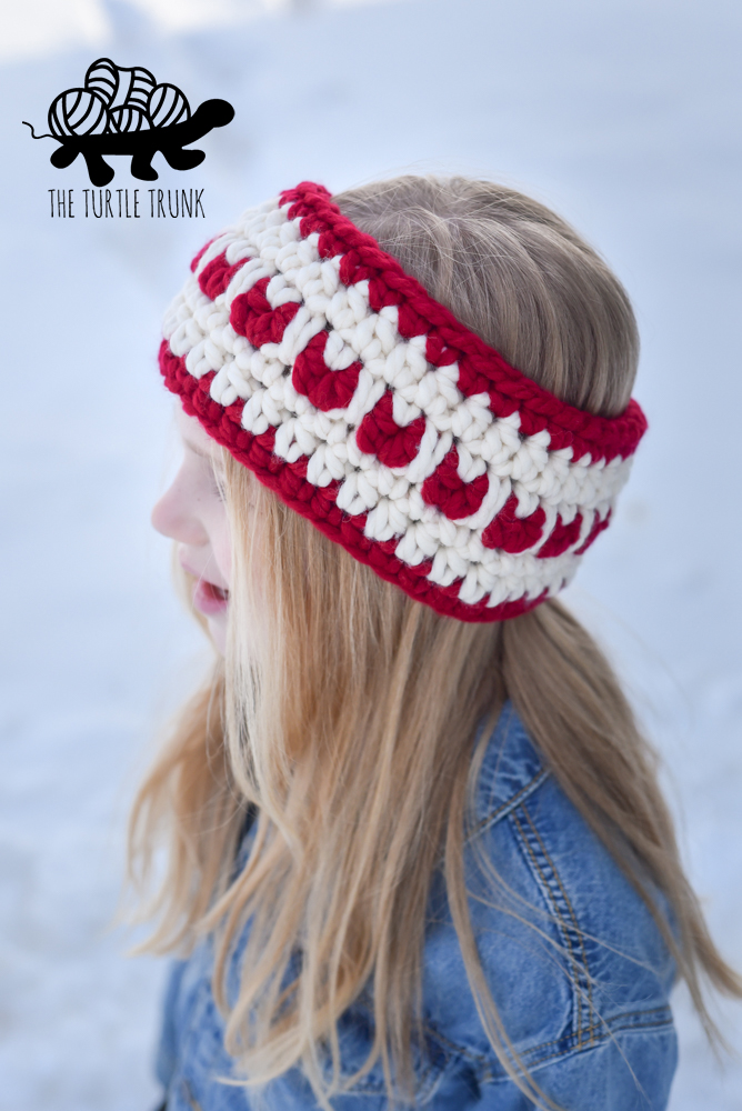 Girl wearing a red and white crochet ear warmer with hearts on it.