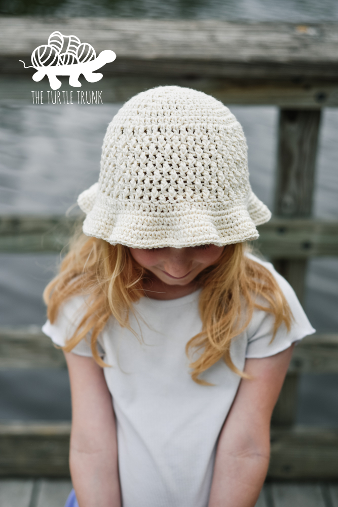 Girl wearing a white, crochet sun hat with a ruffled brim. Crochet pattern is the Country Cottage Sun Hat by The Turtle Trunk.