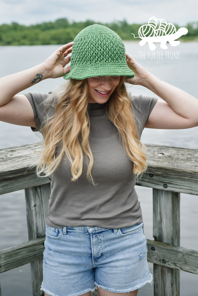 Woman wearing a green, crochet sun hat. Crochet pattern is the Country Cottage Sun Hat by The Turtle Trunk.