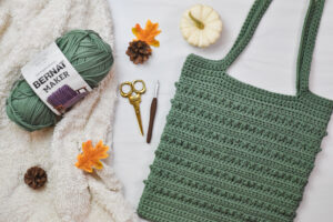 A green, crochet tote bag lays on a white surface. Picot Tote Bag crochet by The Turtle Trunk.