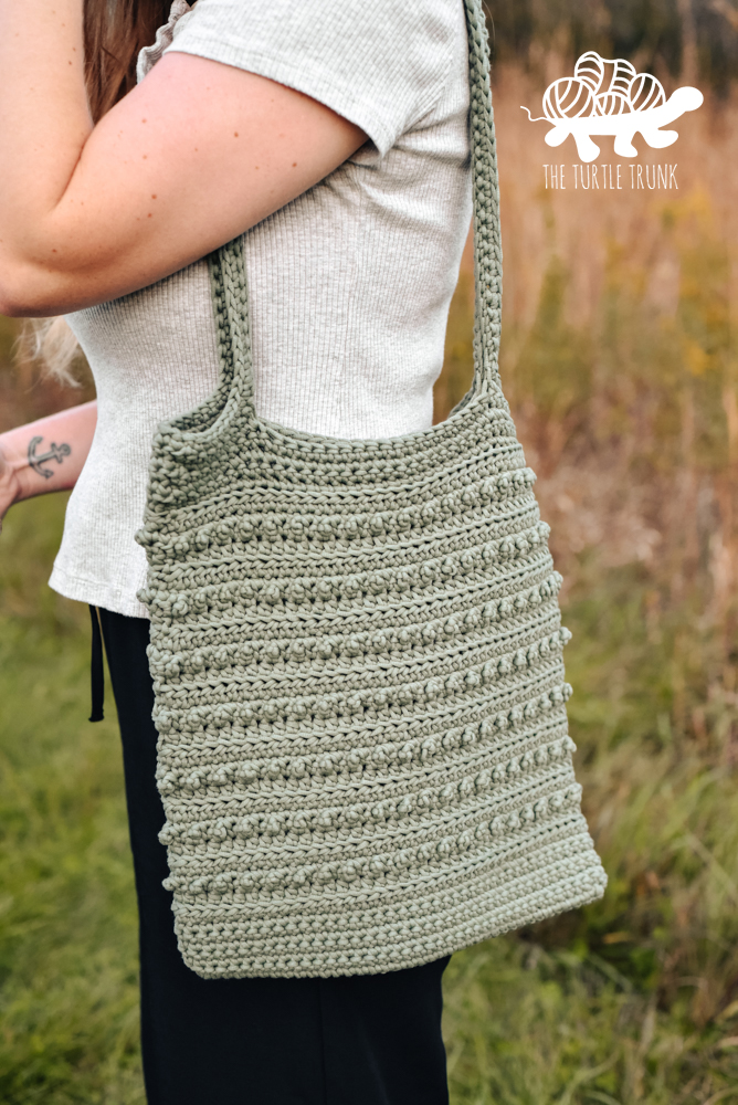 Woman holding a green, crochet tote bag. Crochet pattern is the Picot Tote Bag by The Turtle Trunk.